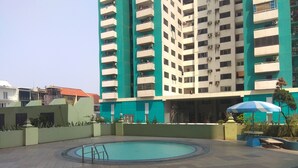 A swimming pool surrounded by a tiled patio area with a blue umbrella and a bench. - New Furnished 1BR Rajawali Apartment (Jakarta)