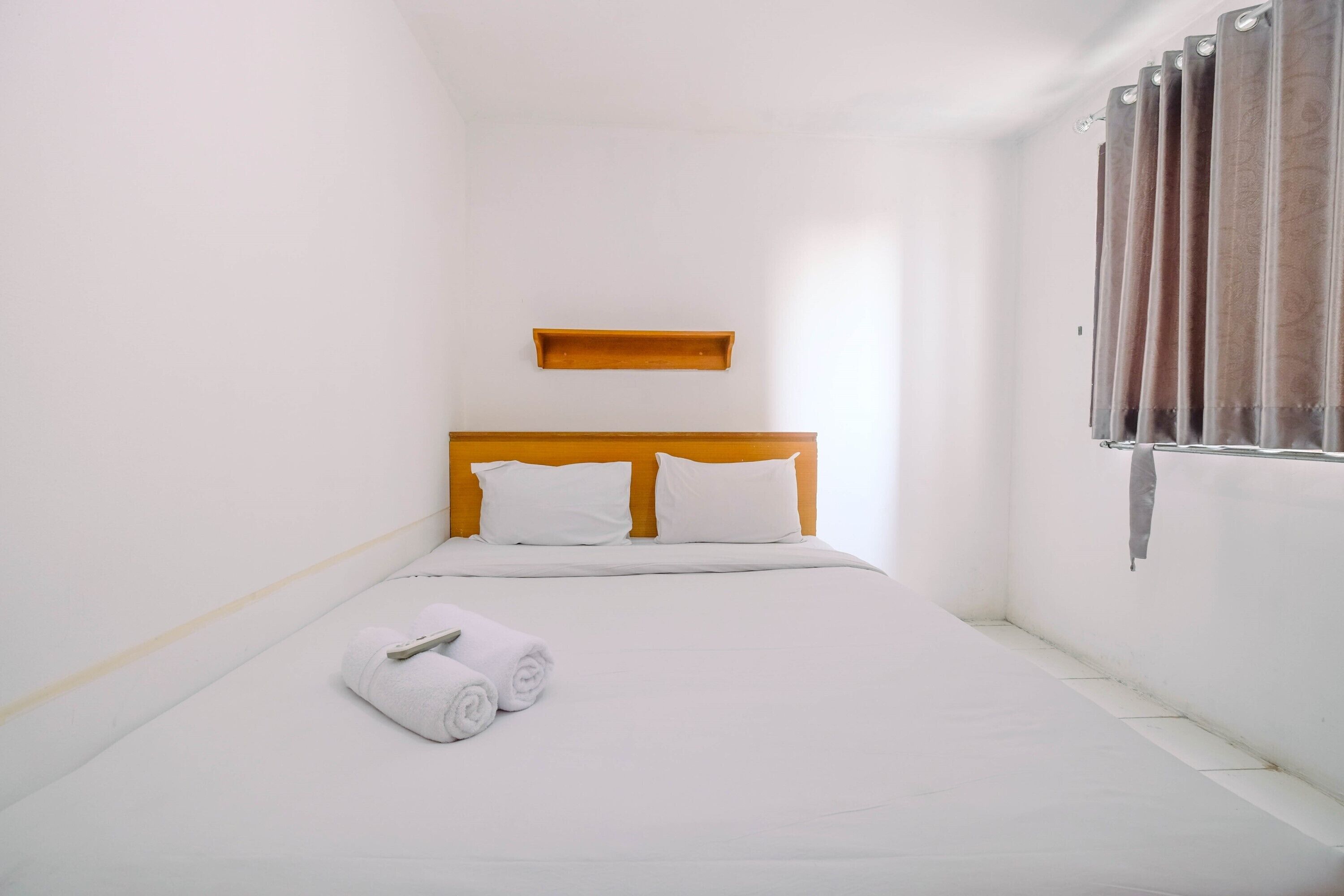 Una habitación pequeña y limpia con una cama individual, ropa de cama blanca, cabecera de madera y una ventana con cortinas.