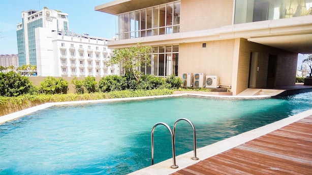 A swimming pool with a wooden deck and metal railings, surrounded by greenery and modern buildings. - Modern and Stylish Studio Apartment at Elpis Residence (Jakarta)