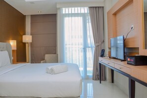 A hotel room with a large bed, a desk with a television, and a view of the city through the window. - Modern and Tidy Studio Apartment at Elpis Residence (Jakarta)
