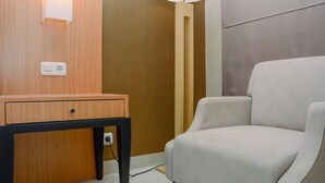 A modern hotel room with a wooden desk, a lamp, and a comfortable chair. - Modern and Tidy Studio Apartment at Elpis Residence (Jakarta)