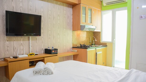 Hotelkamer met een bed, een televisie, een bureau met computer, een klein keukenhoekje en een raam.