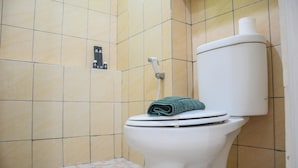 Toilet met een handdoek op de zitting, een toiletrolhouder en een douchetoilet in een betegelde badkamer.