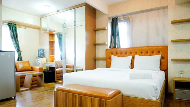 Camera d'albergo con un letto grande, una panca di legno, una scrivania, una sedia, un armadio e un dispenser d'acqua.