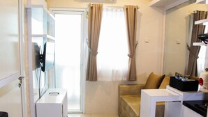 Ein kleines Hotelzimmer mit einer Couch, einem Tisch, einem Fernseher und einer Tür zum Balkon.