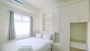 Quarto bem arrumado com cama, mesa de cabeceira, guarda-roupa e janela com cortinas.