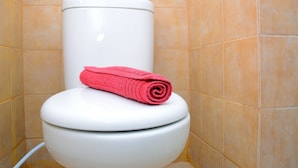 Een wit toilet met een roze handdoek erop, voor een betegelde muur.