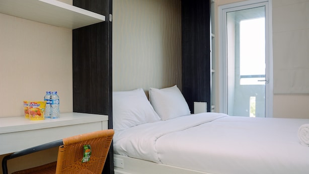 Een hotelkamer met een bed, een bureau met stoel, een klein plankje met spullen en een deur naar een balkon.