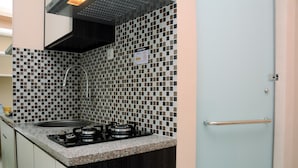 Een keuken met een betegelde achterwand, een gasfornuis, een spoelbak en een deur met een handvat.