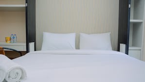 Een net opgemaakt bed met witte lakens, een opgerolde witte handdoek en een tafeltje met twee waterflesjes en een bakje.