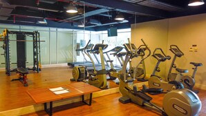 Une salle de sport équipée de divers appareils d’exercice, notamment des tapis de course et des appareils de musculation, ainsi qu’un banc en bois.