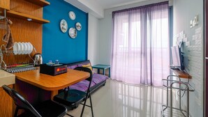 Una habitación compacta con un escritorio de madera, una cama con colcha morada, pared azul y ventana con cortinas moradas.