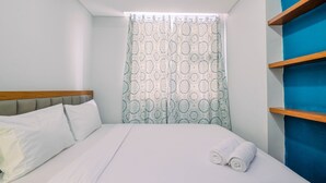 Habitación de hotel con cama, cabecero, ventana con cortinas estampadas y pared azul con estante.