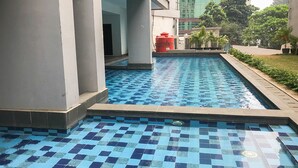 Piscina con azulejos azules y blancos, rodeada por un muro bajo y una zona ajardinada con plantas en macetas.