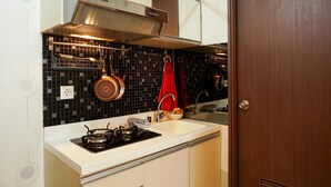 A kitchen with a gas stove, a sink, and a backsplash of black tiles. - Functional and Compact 1BR Belmont Apartment (Jakarta)