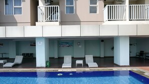 A swimming pool area with lounge chairs and a view of a building with balconies. - Functional and Compact 1BR Belmont Apartment (Jakarta)
