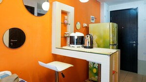 A compact kitchen with a white countertop, a coffee maker, a kettle, and a refrigerator. - Functional and Compact 1BR Belmont Apartment (Jakarta)