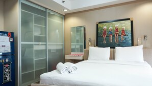 Een hotelkamer met een bed, een glazen inloopkast, een schilderij aan de muur en een klein tafeltje met een roze voorwerp.