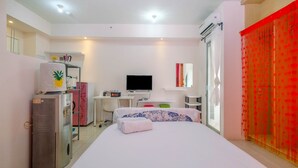 A hotel room with a bed, a desk, a television, a wardrobe, and a minibar. - Modern and Comfort Stay @ Studio Pakubuwono Terrace Apartment (Jakarta)