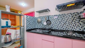 A compact kitchen with a black countertop, pink cabinets, a stainless steel kettle, a gas stove, and a tiled backsplash. - Modern and Comfort Stay @ Studio Pakubuwono Terrace Apartment (Jakarta)