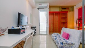 A clean, modern living room with a white sofa, a flat-screen TV, a desk with a computer, and a large window. - Modern and Comfort Stay @ Studio Pakubuwono Terrace Apartment (Jakarta)