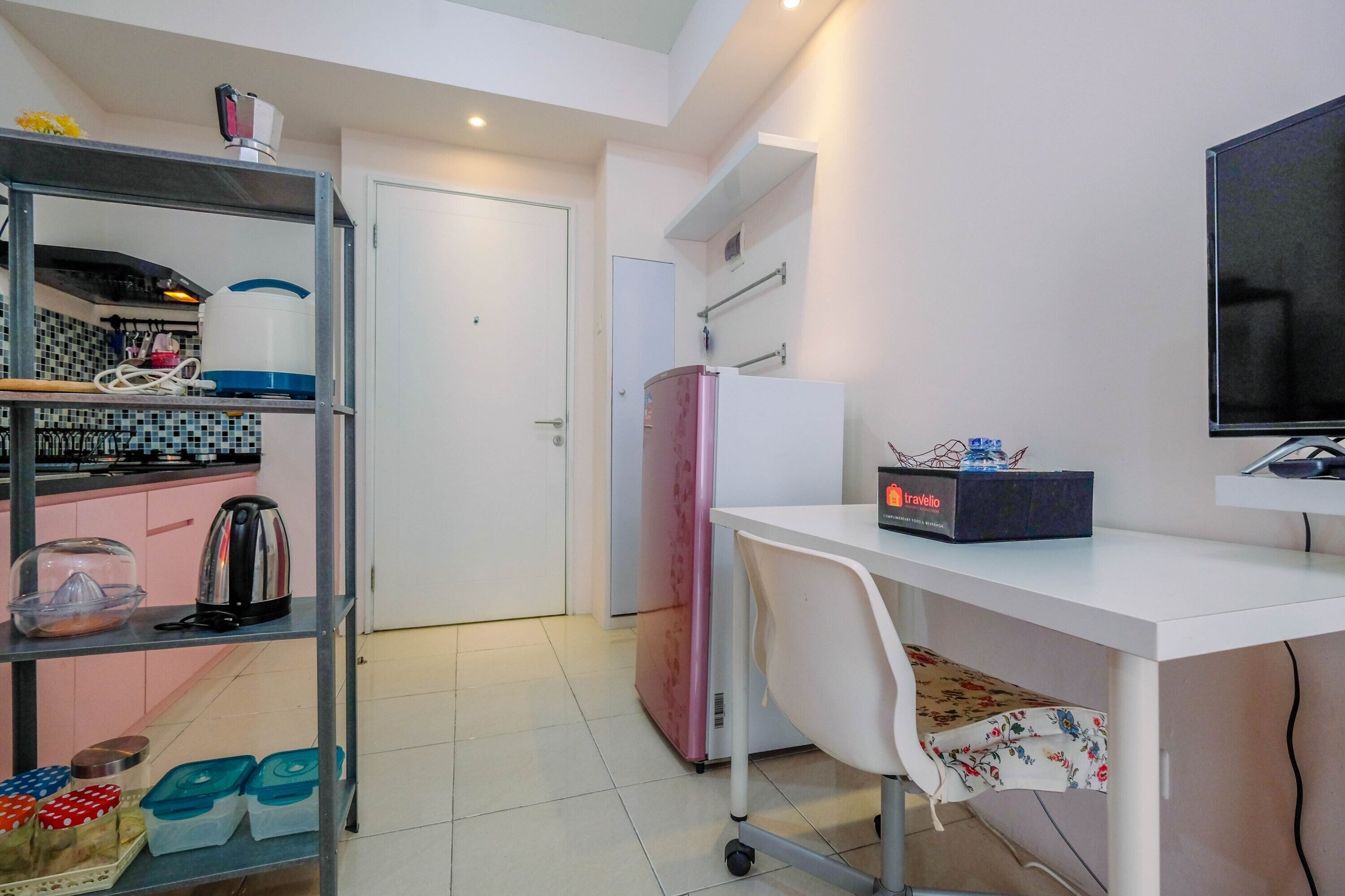 A compact kitchen with a sink, stove, and a pink refrigerator. There's a white desk with a chair and a flat-screen TV.