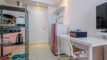 A compact kitchen with a sink, stove, and a pink refrigerator. There's a white desk with a chair and a flat-screen TV.