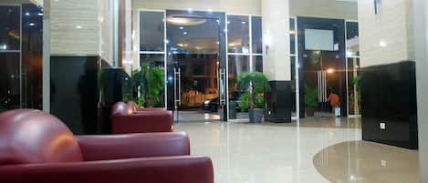 A modern lobby with a reception desk, seating area, and potted plants.