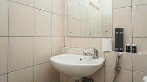 Un baño con lavamanos blanco, un espejo y una ducha. Hay artículos de aseo en la pared.