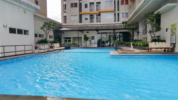 Una piscina con zona cubierta y un edificio al fondo.