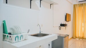 Una cocina con un lavabo, un escurreplatos, un refrigerador pequeño y un televisor montado en la pared.