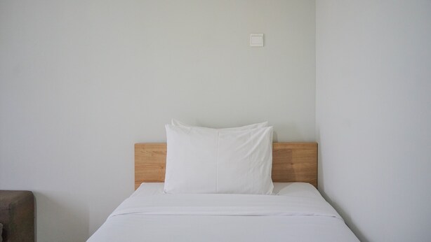 A simple, unadorned bed with a wooden headboard and white bedding in a minimalistic room. - Minimalist Studio at Beverly 90210 Apartment (Gading Serpong)