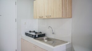 A small kitchen with a built-in gas stove, a sink, and wooden cabinets. - Minimalist Studio at Beverly 90210 Apartment (Gading Serpong)
