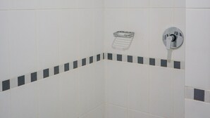 A bathroom with white tiled walls, a shower with a handheld showerhead, and a towel rack. - Minimalist Studio at Beverly 90210 Apartment (Gading Serpong)