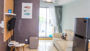 Un espace de vie compact comprenant un canapé, une petite table, un réfrigérateur, un téléviseur fixé au mur et une fenêtre avec des rideaux.