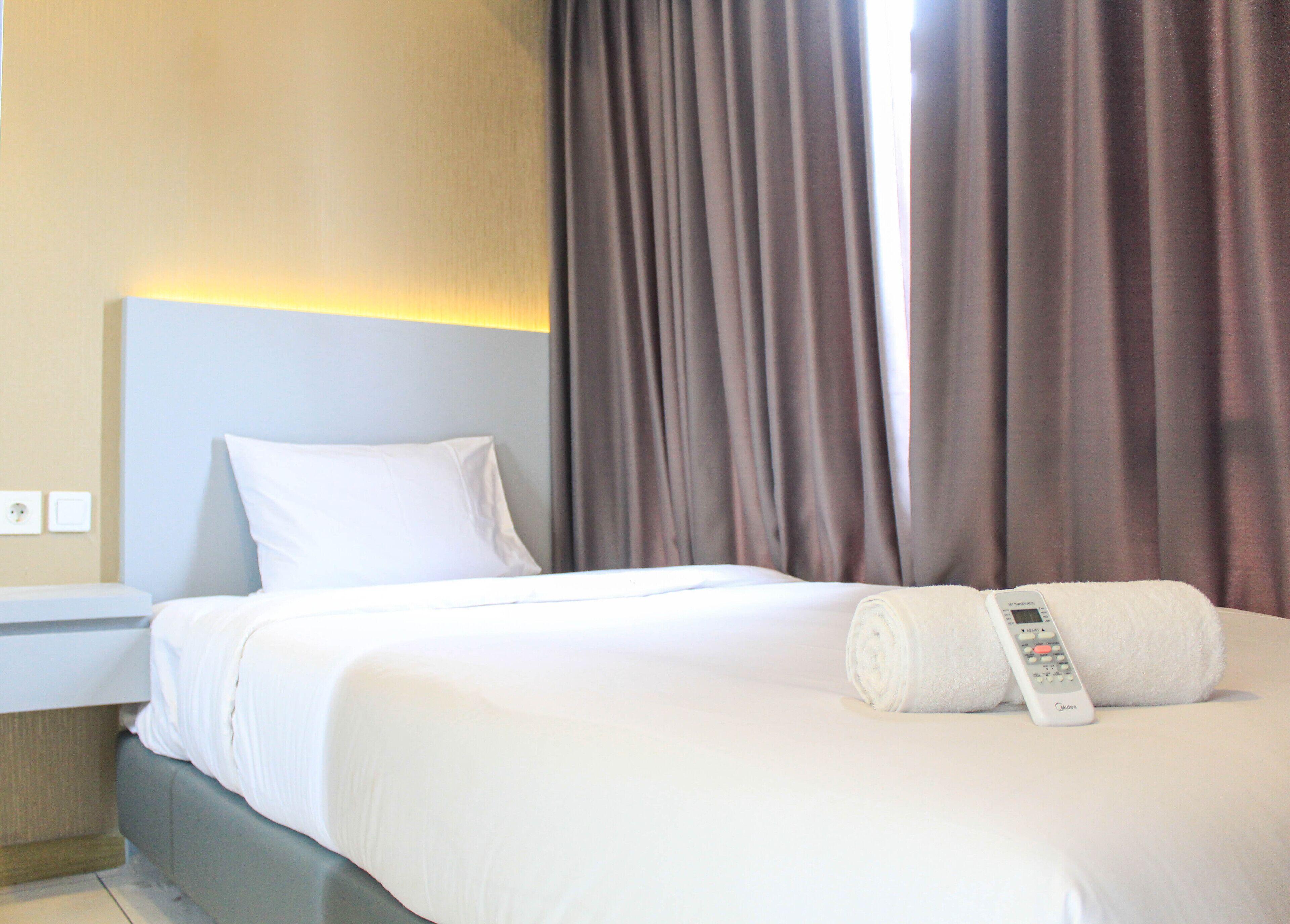 A hotel room with a neatly made bed, a remote control on the bed, and a nightstand with a lamp.
