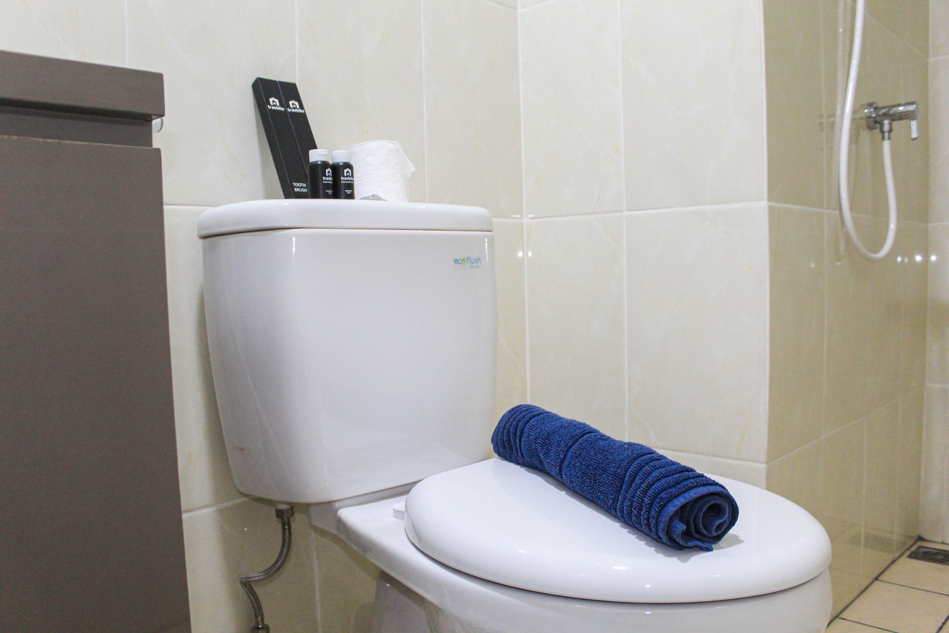 Inodoro blanco con una toalla azul sobre el asiento, un tirador de la cadena y un rollo de papel higiénico.