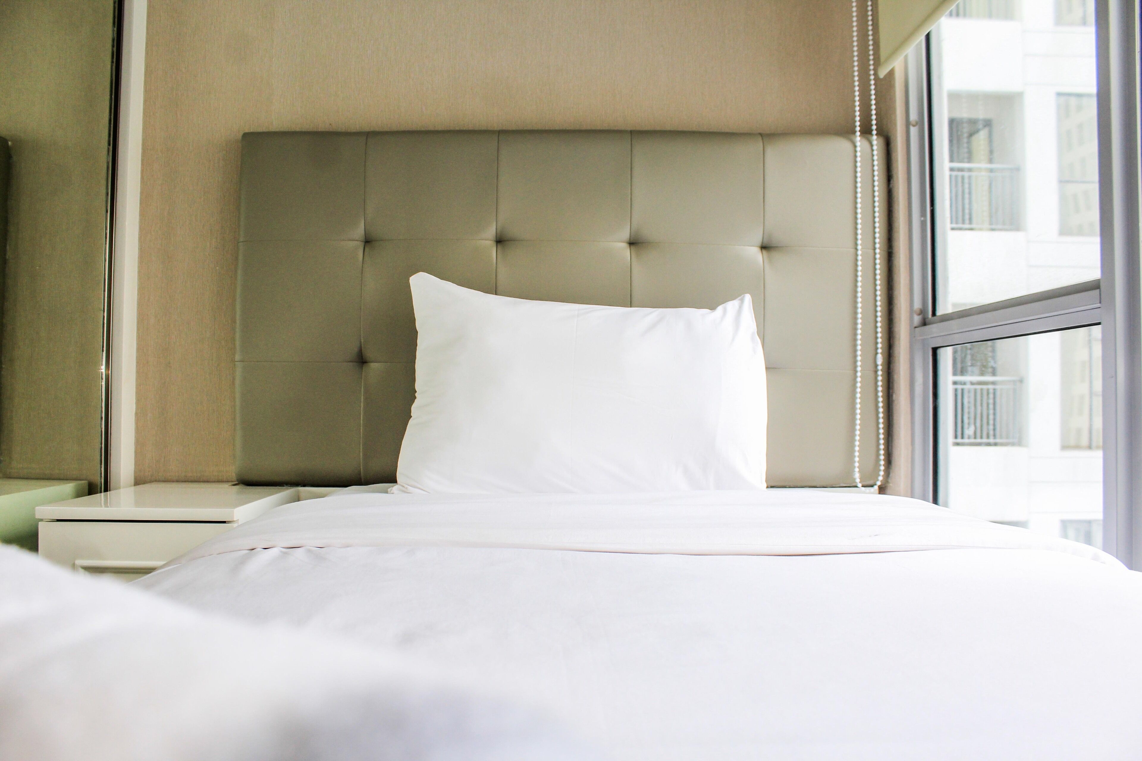 A neatly made bed with a tufted headboard, a white pillow, and a white bedspread.