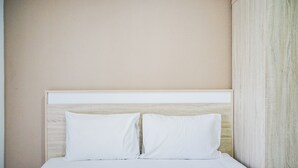 A neatly made bed with white linens and pillows, a wooden headboard, and a plain wall. - Minimalist and Comfy Studio Springwood Apartment (Tangerang)
