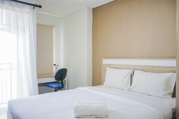 A hotel room with a bed, a chair, a desk, and a window with curtains. - Minimalist and Comfy Studio Springwood Apartment (Tangerang)