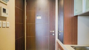 A kitchen with a wooden door, a stainless steel sink, and a wall-mounted thermostat. - Compact and Cozy Studio Atria Apartment (Gading Serpong)