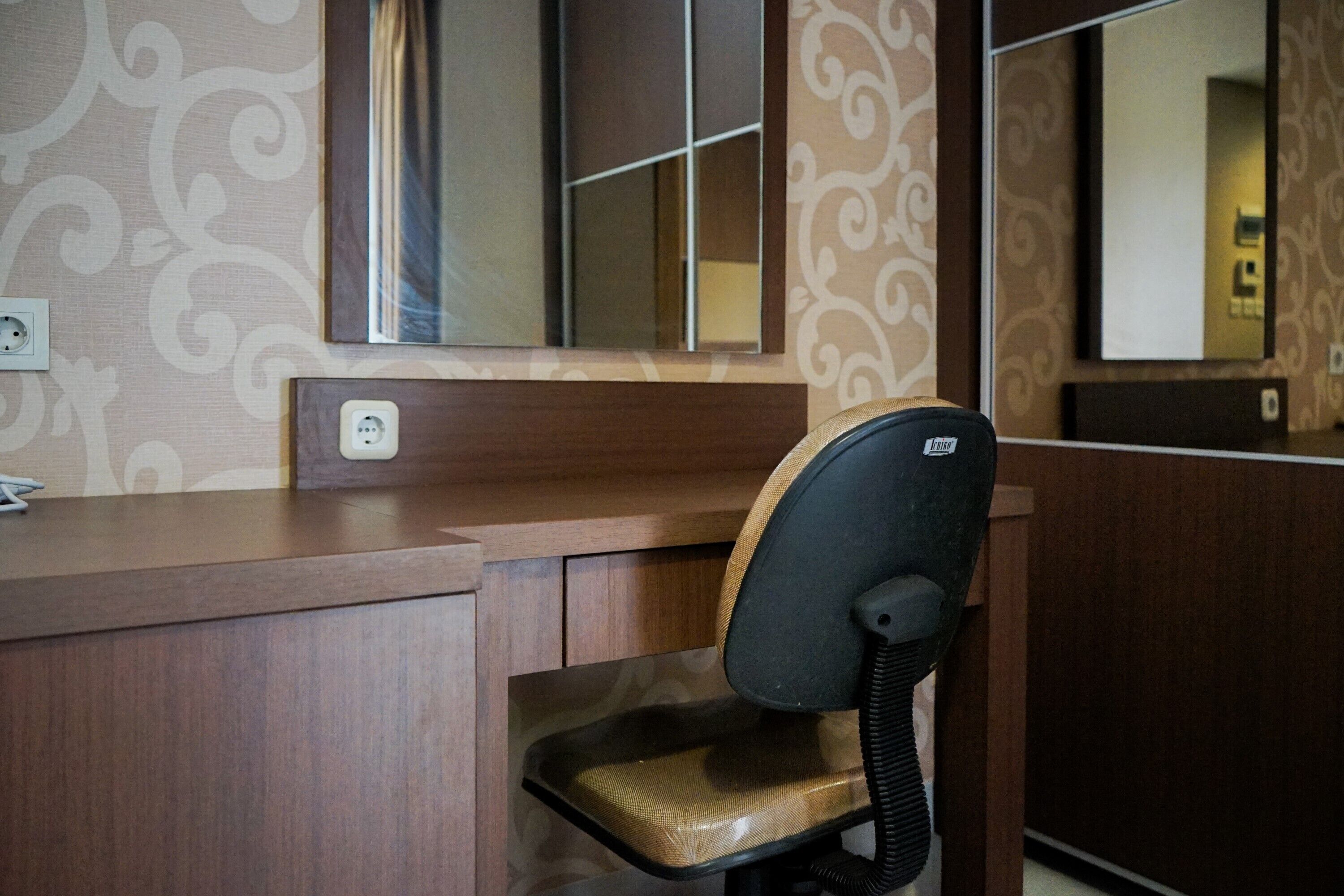 Habitación de hotel con un escritorio de madera, una silla, un espejo y un enchufe.