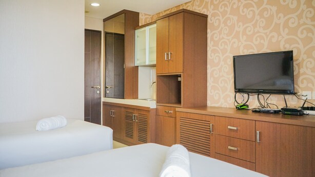 A hotel room with two beds, a television, wooden cabinets, and a mirror. - Compact and Cozy Studio Atria Apartment (Gading Serpong)