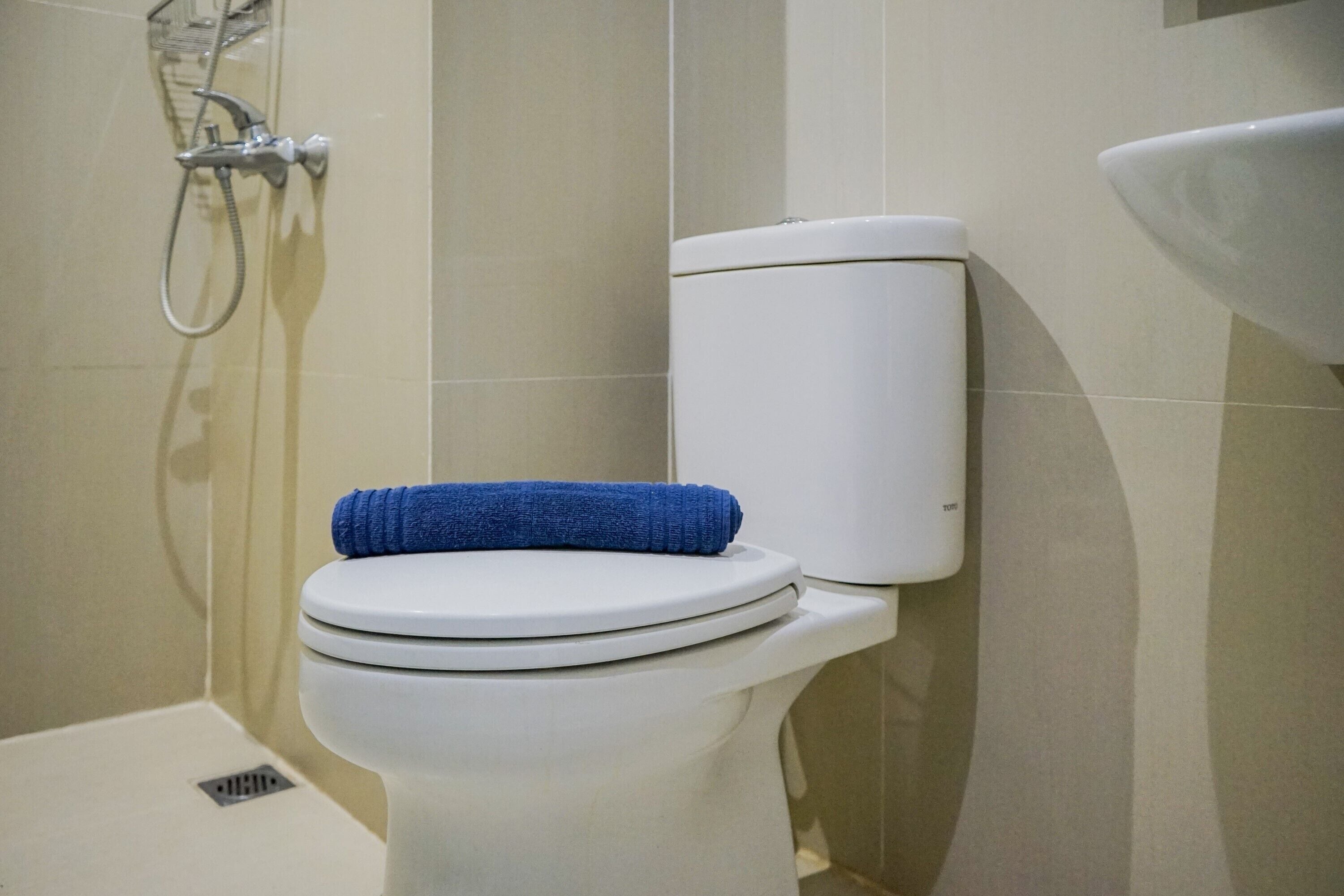 A white toilet with a blue towel on the seat, a showerhead, and a sink.