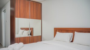 Habitación de hotel con un armario de madera, una cama con ropa de cama blanca y un espejo grande que refleja la cama y el armario.