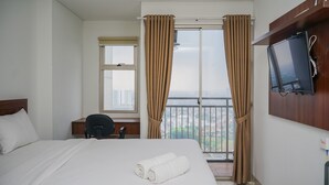 Habitación de hotel con cama, escritorio, silla, televisor montado en la pared y balcón con cortinas.