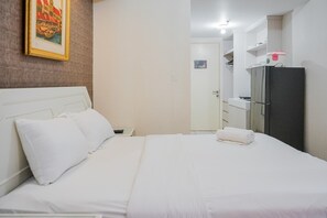 Habitación de hotel con cama, mesita de noche, refrigerador y puerta de baño.