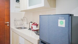Uma cozinha com armários brancos, uma pia de aço inoxidável, uma chaleira elétrica vermelha e branca e uma geladeira prateada com o logotipo 'SHARP'.