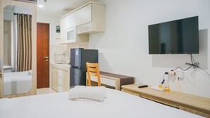 Quarto de hotel com cama, escrivaninha, cadeira, televisão e minibar.