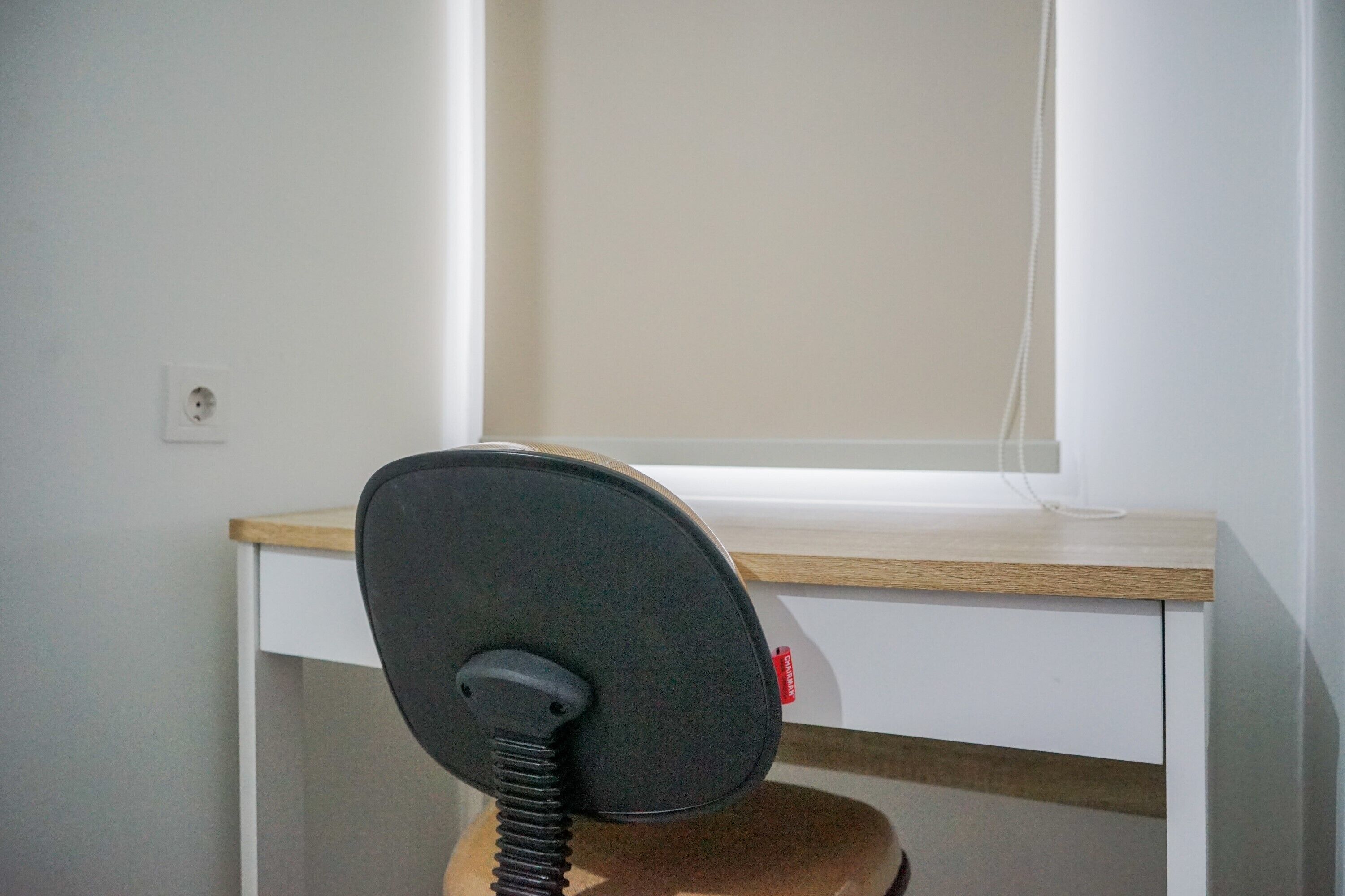 A chair with a headrest and a desk with a light wooden top and white drawers.